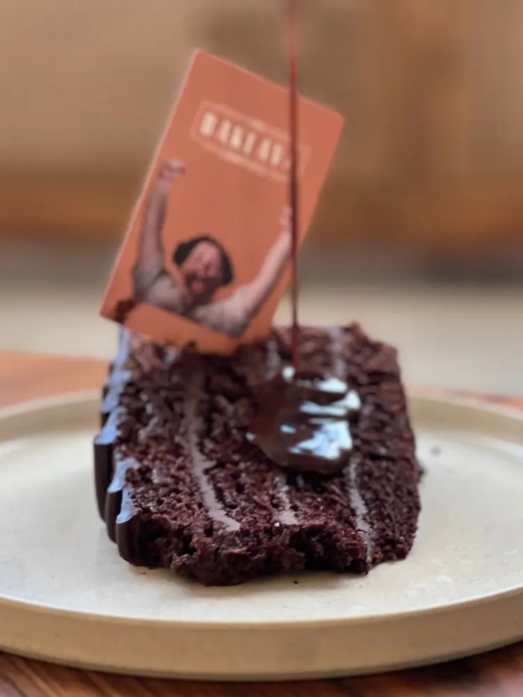 Slice of chocolate fudge cake on a cream plate with warm chocolate sauce being poured over it